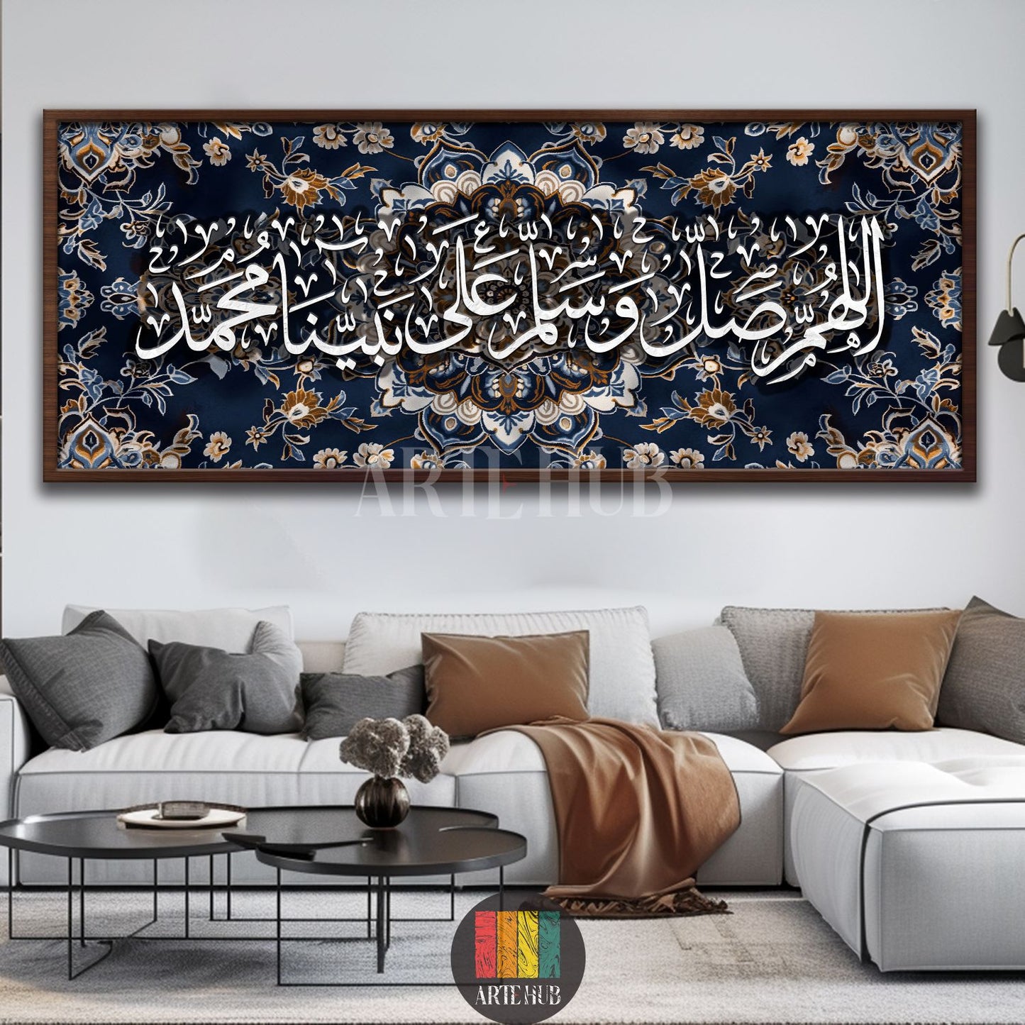 Long rectangular Islamic calligraphy canvas featuring "اللهم صل وسلم على نبينا محمد" in elegant white script, set against a dark blue background with intricate gold and blue floral patterns. The canvas is framed in dark wood and displayed prominently above a modern white sectional sofa with grey and brown cushions in a contemporary living room setting in Egypt. Two black coffee tables are in front of the sofa, enhancing the stylish Egyptian home decor.
لوحة قماشية مستطيلة طويلة لفن الخط الإسلامي بعبارة "الل