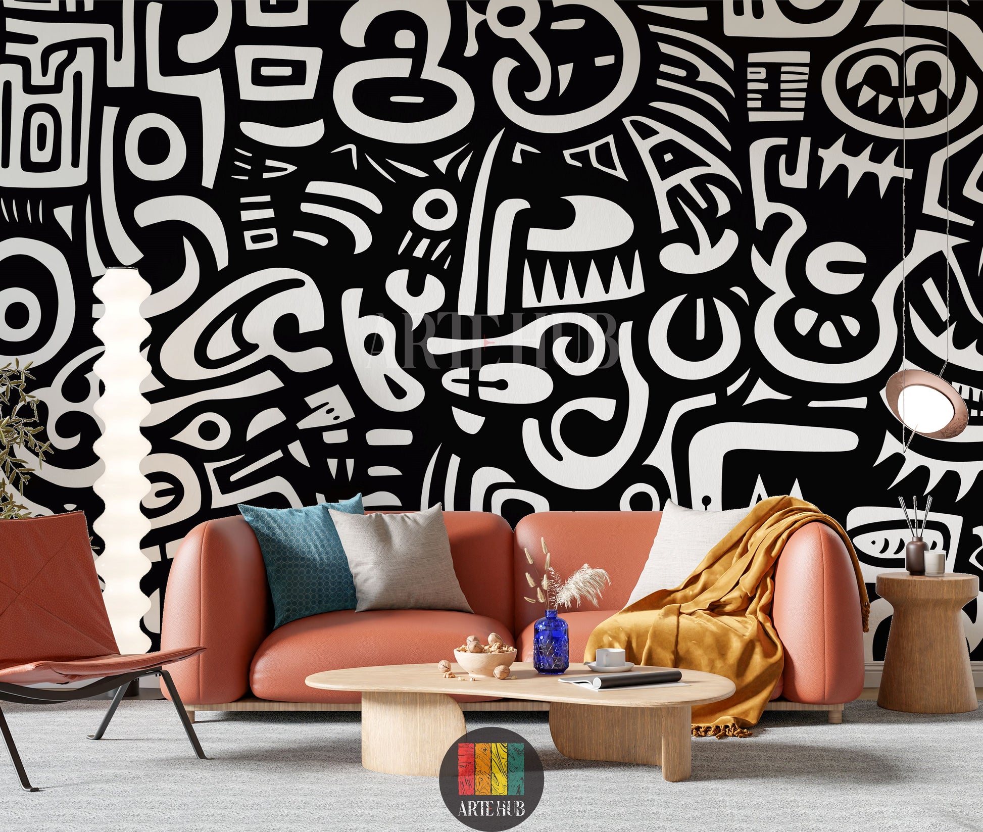 A modern living room featuring a striking black and white abstract wallpaper with bold, flowing graffiti-style patterns. An orange leather sofa with blue and grey cushions, a light wooden coffee table, and a brown leather lounge chair are arranged on a light grey rug. A tall white floor lamp and a unique copper pendant light illuminate the artistic space.
غرفة معيشة عصرية تضم ورق حائط تجريدي مذهل بالأبيض والأسود بنقوش جريئة على طراز الجرافيتي. تظهر أريكة جلدية برتقالية مع وسائد زرقاء ورمادية، وطاولة قهوة خش