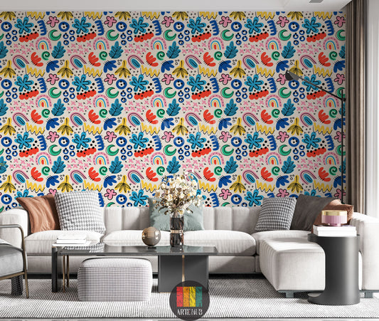  A vibrant living room featuring a wall covered in Whimsical Abstract Colorful Wallpaper. The pattern includes hand-drawn shapes like flowers, leaves, rainbows, squiggles, and dots in bright blues, reds, yellows, pinks, and greens on a light background. A modern grey sectional sofa with various pillows, a black coffee table, and a black floor lamp are visible in the foreground.
 غرفة معيشة مشرقة تتميز بجدار مغطى بورق حائط تجريدي ملون مرح. يظهر النمط رسومات يدوية لأشكال مثل الزهور والأوراق وأقواس قزح و