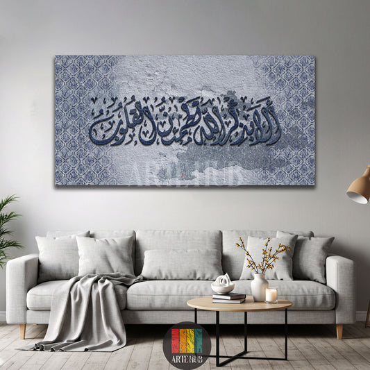Blue Arabic calligraphy canvas «ألا بذكر الله تطمئن القلوب» with a grey textured background above a light grey sofa, Artehub Egypt.