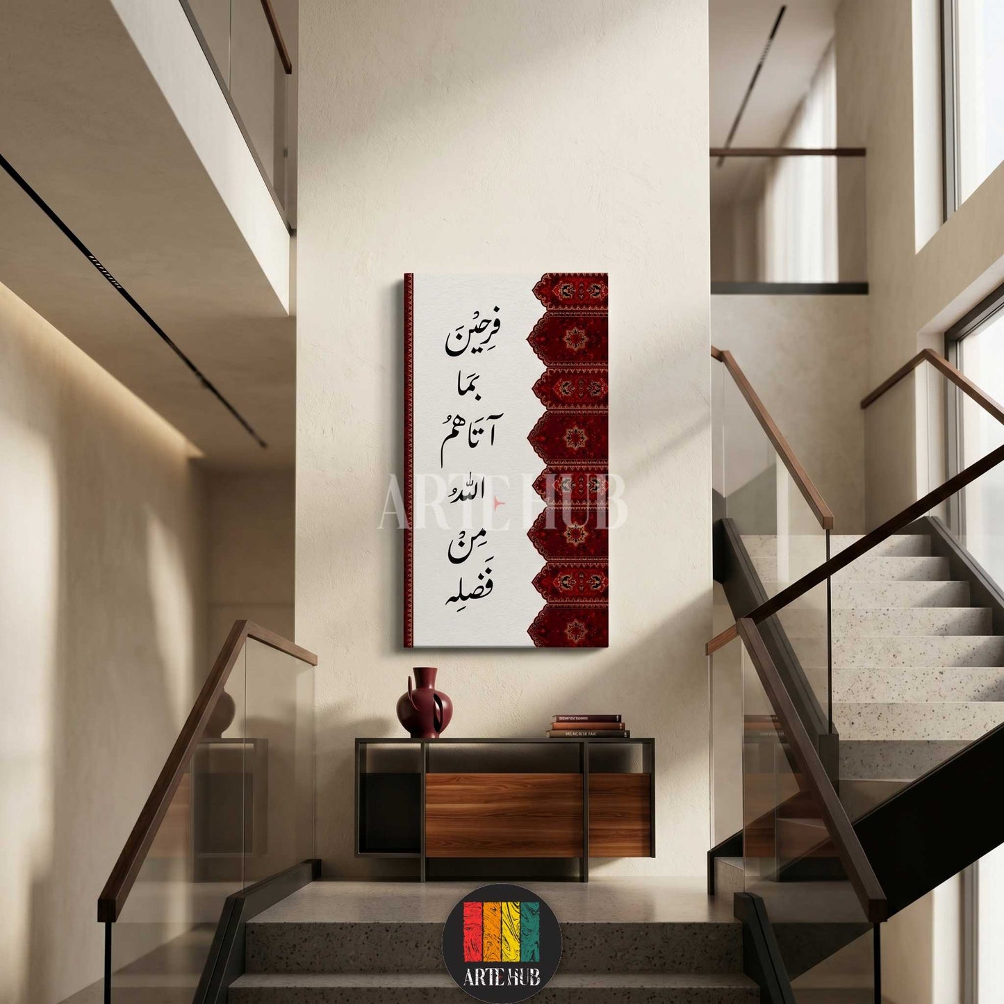 A vertical canvas wall art displaying elegant Arabic calligraphy with a red traditional patterned border, hung in a modern minimalist interior with stairs.