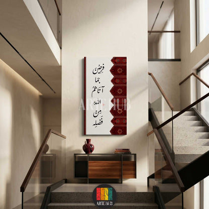 A vertical canvas wall art displaying elegant Arabic calligraphy with a red traditional patterned border, hung in a modern minimalist interior with stairs.