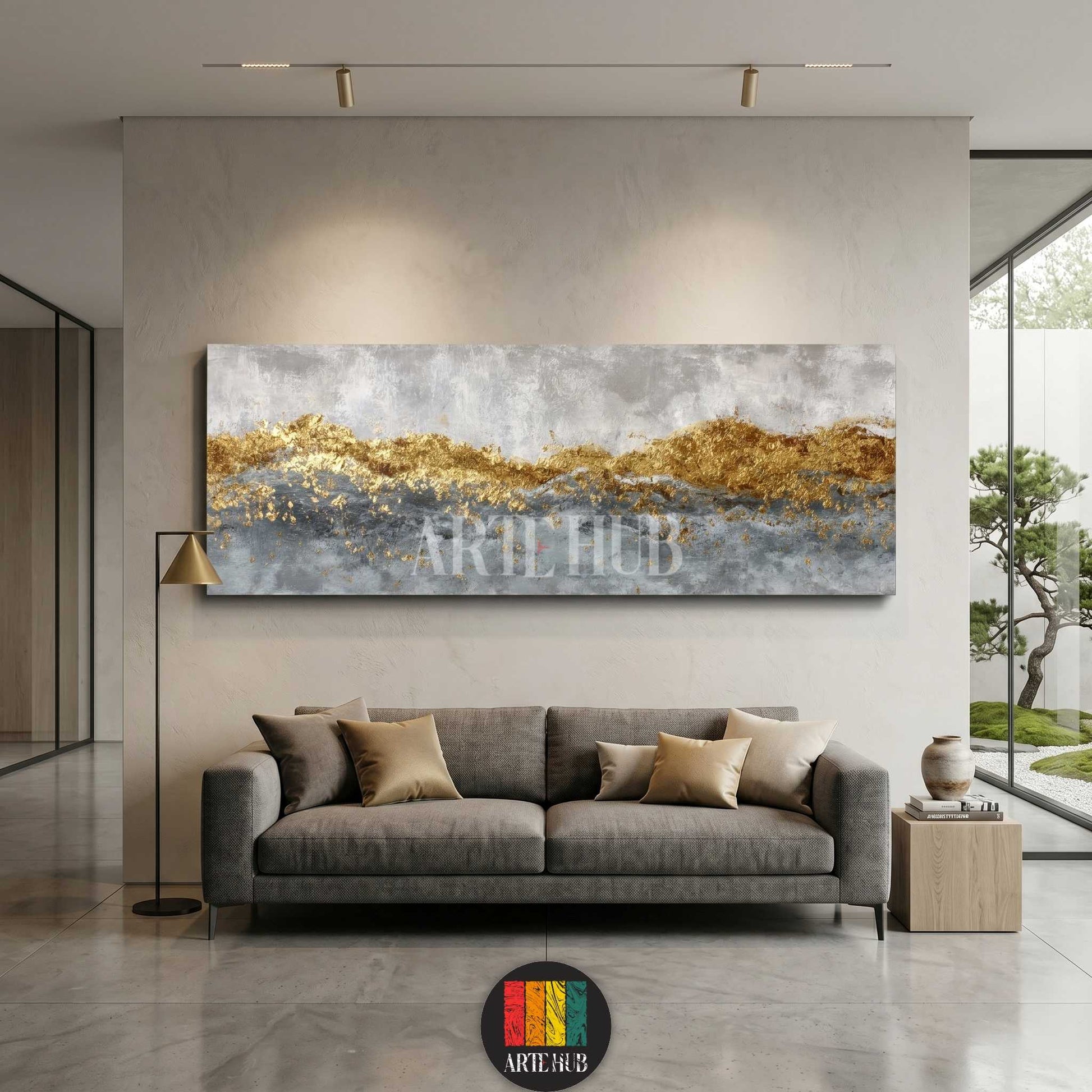 Horizontal abstract canvas wall art with gold leaf mountain-like texture and grey tones hung above a contemporary sofa in a high-end living room.