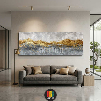 Horizontal abstract canvas wall art with gold leaf mountain-like texture and grey tones hung above a contemporary sofa in a high-end living room.