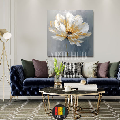 A luxury square canvas wall art piece displaying a stylized white flower with golden highlights on a textured grey background in a modern living room.