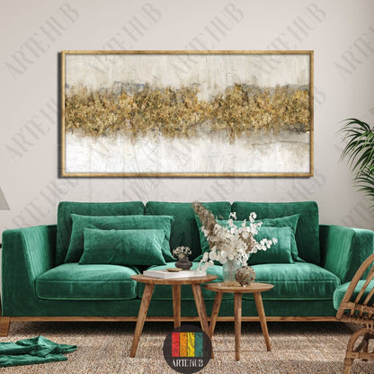 A horizontal luxury canvas wall art featuring abstract gold foil textures and gray tones in a thin gold frame, styled above a green velvet sofa.
