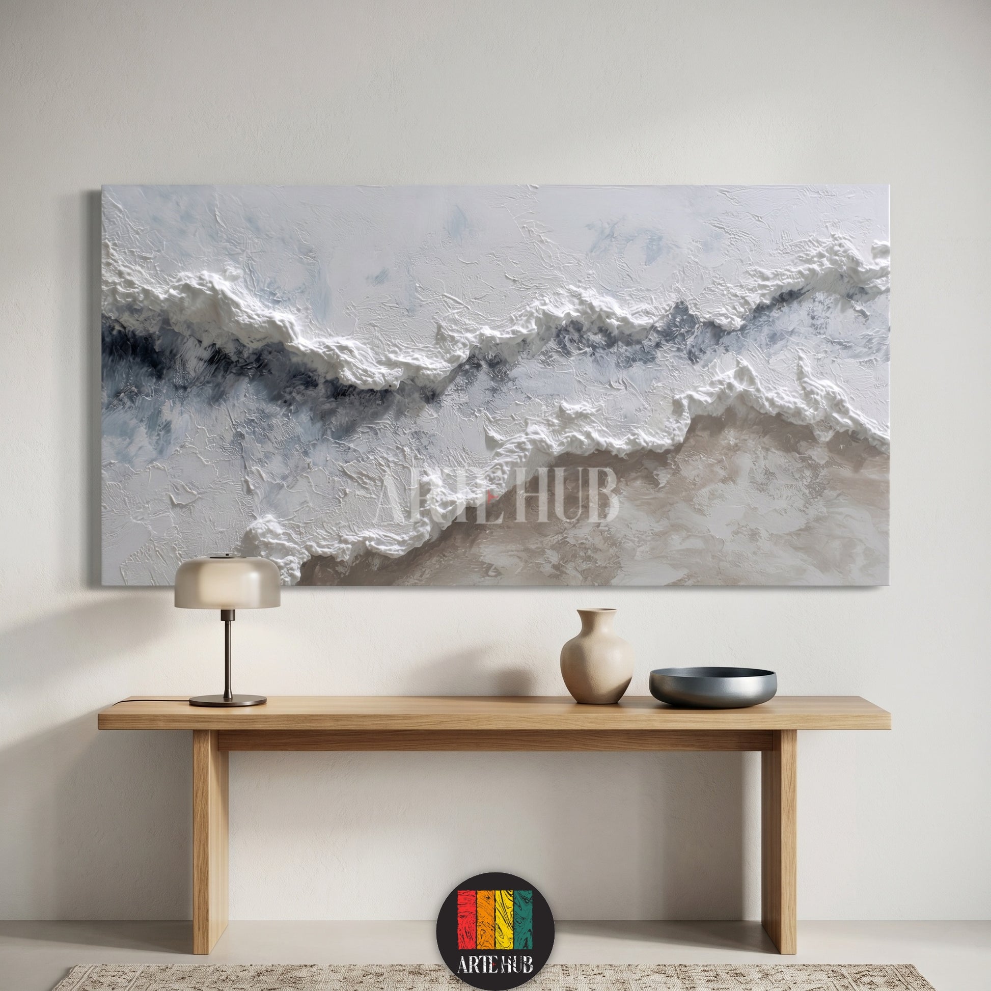 A large horizontal 3D textured abstract canvas wall art depicting crashing white ocean waves in a minimalist room above a wooden console table.